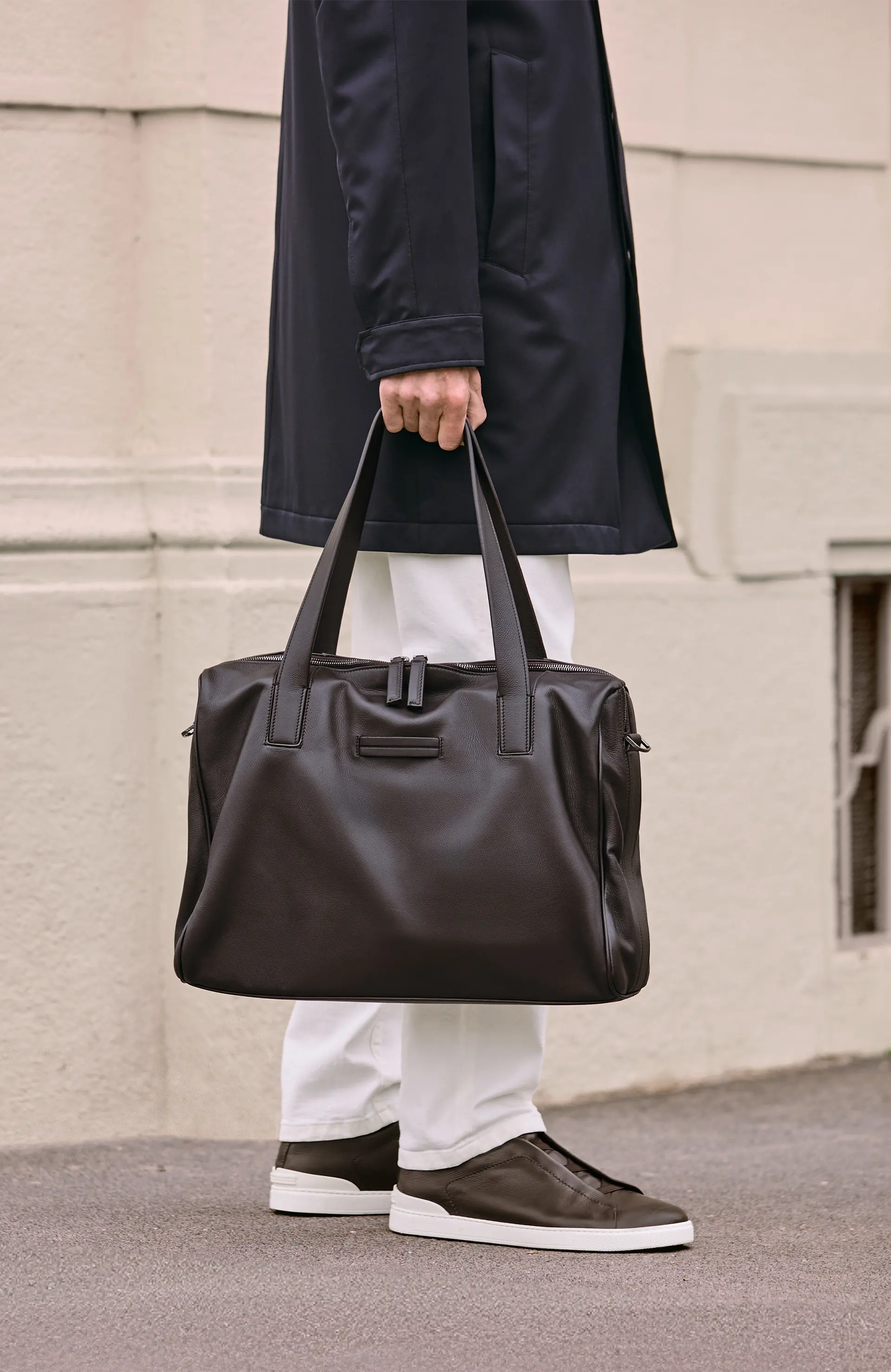 Man carrying a luxury leather bag styled with a trench coat, from the ZEGNA Fall/Winter 2025 collection.