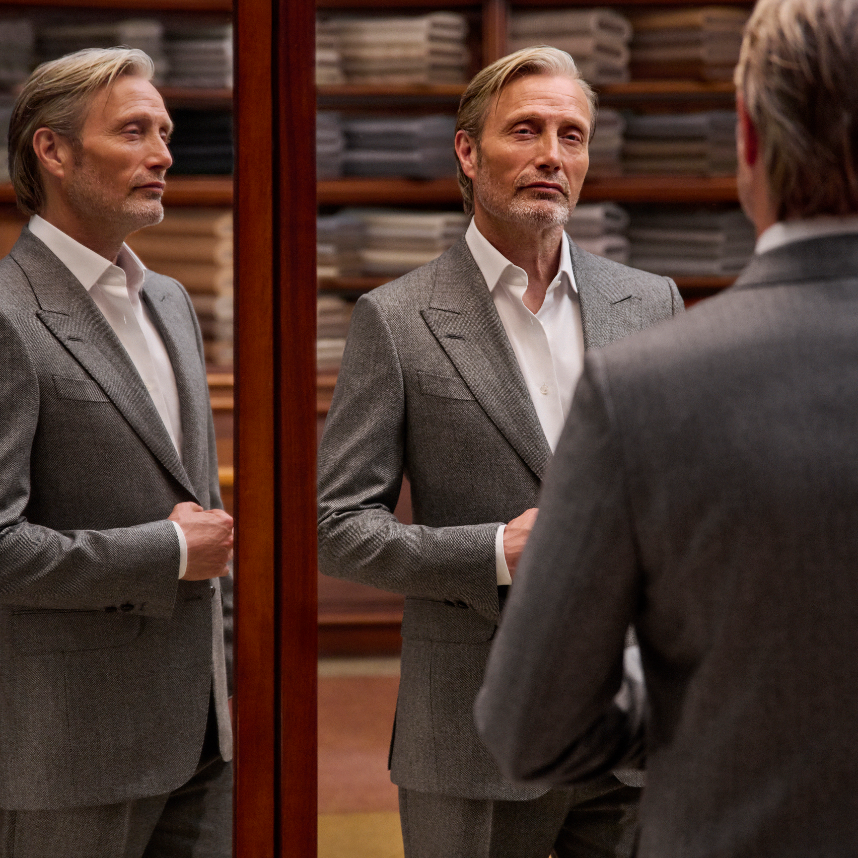 Mads Mikkelsen in a refined grey tailored suit with a white shirt, seen in full in the triple mirror of a tailoring atelier, from the ZEGNA Fall/Winter 2026 collection.