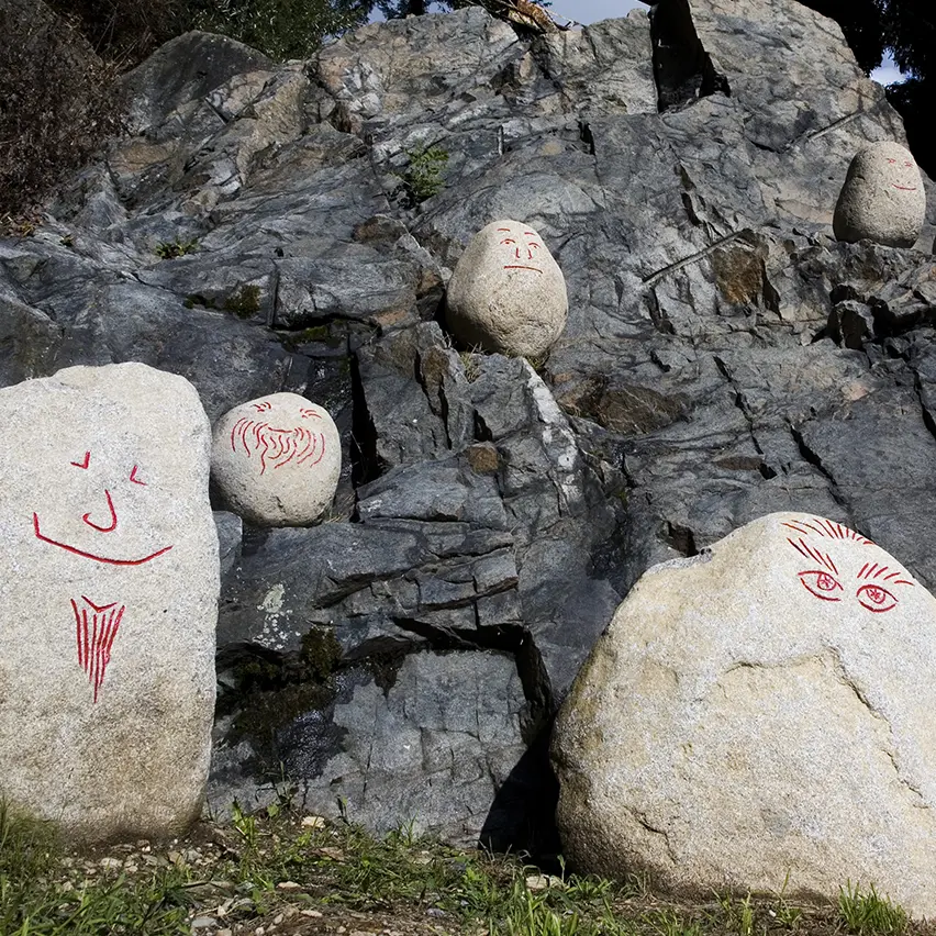 White rocks with faces drawn on them in red marker, placed on top of other rocks, part of Stefano Arienti's 'I Telepati'.