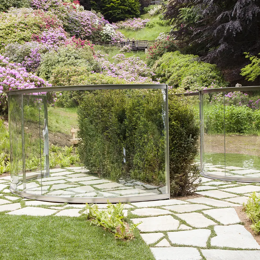 A reflective glass structure with two-way mirrors, set within a landscaped garden.