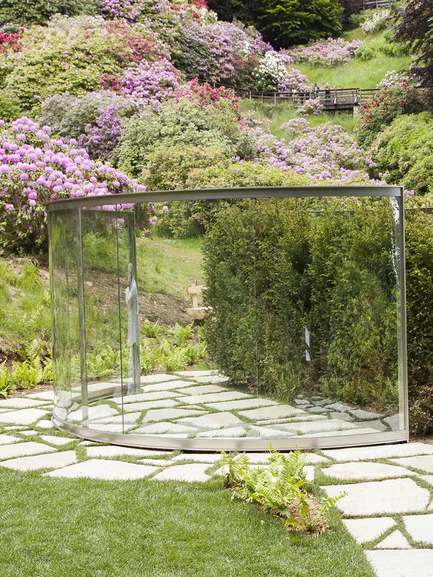 A reflective glass structure with two-way mirrors, set within a landscaped garden.