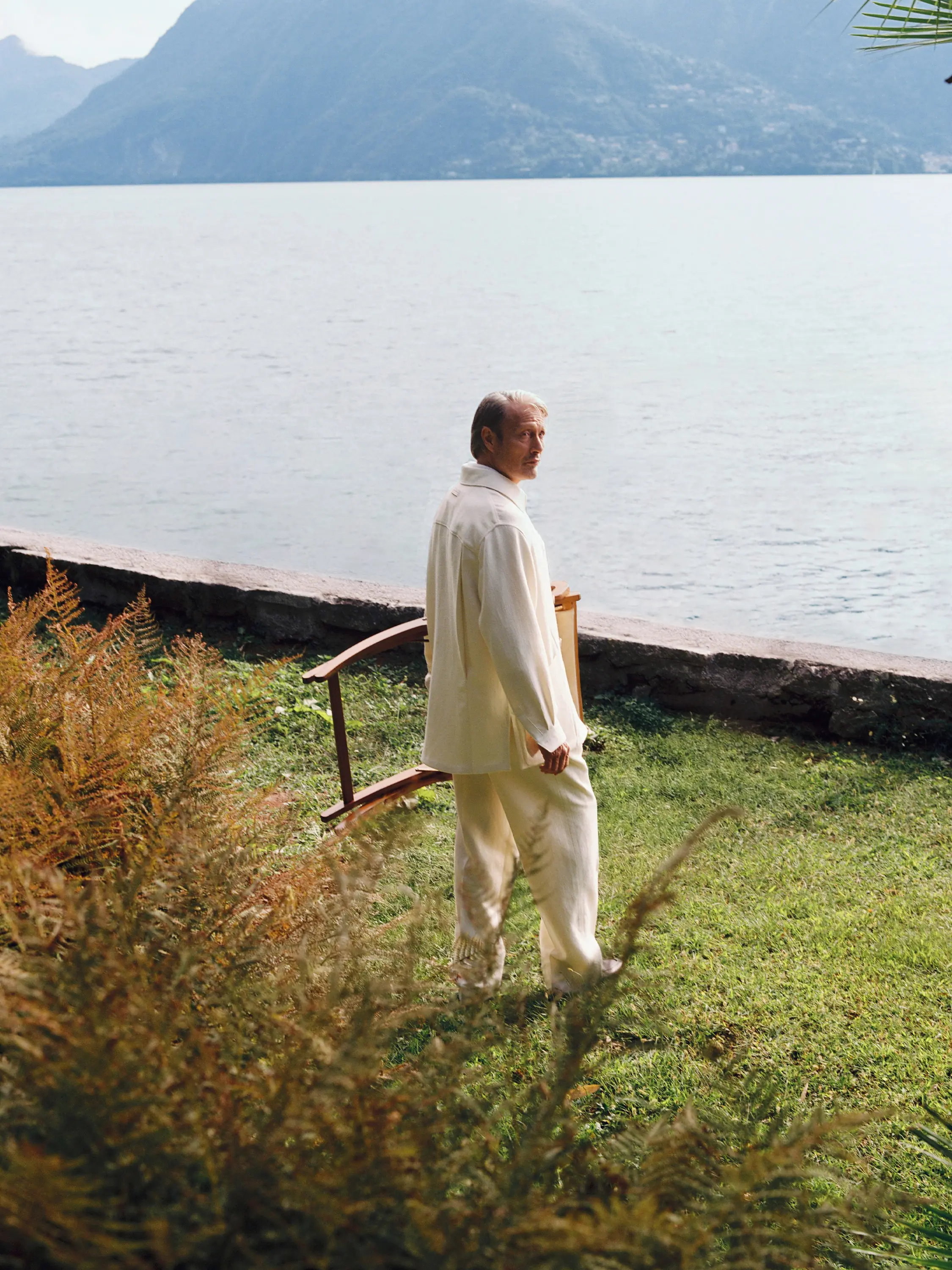 Mads Mikkelsen wearing a refined look from the ZEGNA Spring Summer 2026 collection in a lakeside garden setting.