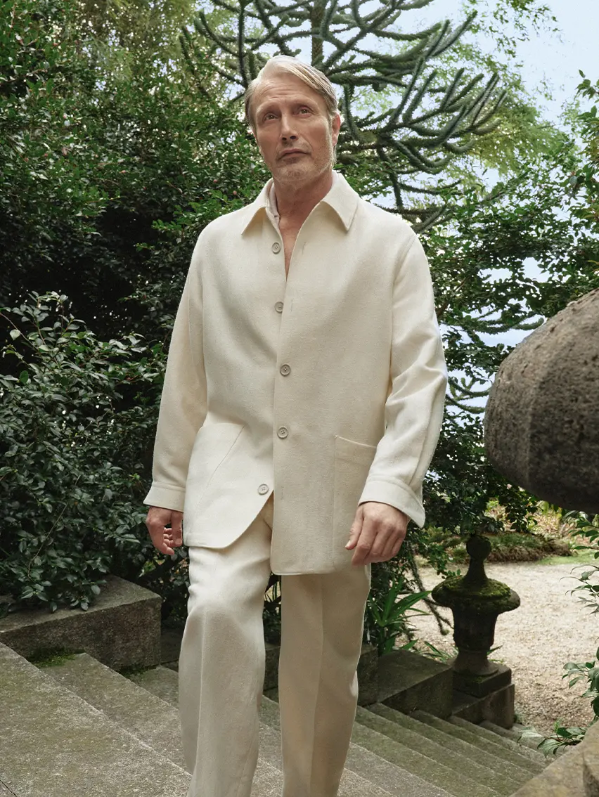 Mads Mikkelsen wearing a refined look from the ZEGNA Spring Summer 2026 collection in a lakeside garden setting.