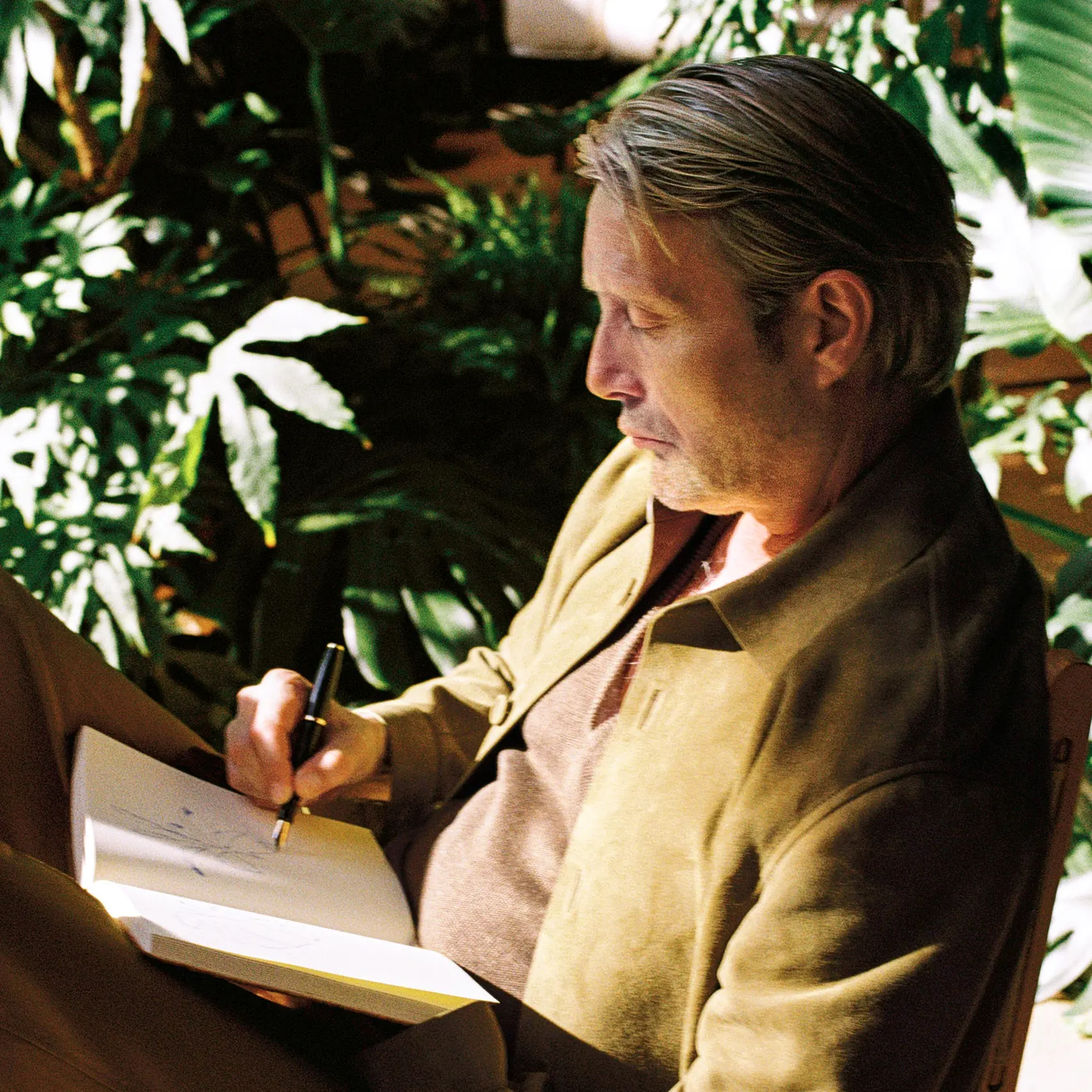 Mads Mikkelsen com um conjunto da coleção Primavera/Verão 2026 da ZEGNA, a esboçar ideias num caderno num momento de criatividade tranquilo.