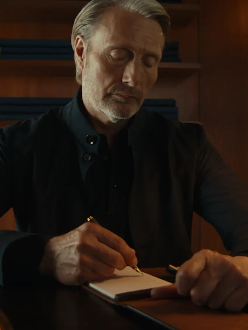 Mads Mikkelsen writing a personal note at a desk.