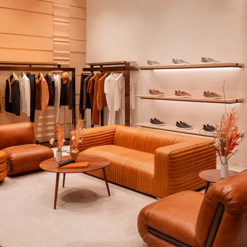 Luxuriöser Herren-Store mit einem weißen Teppich und Ledersesseln. In den Regalen stehen ZEGNA Sneaker und an einem Ständer hängen stilvoll Jacken und Mäntel.