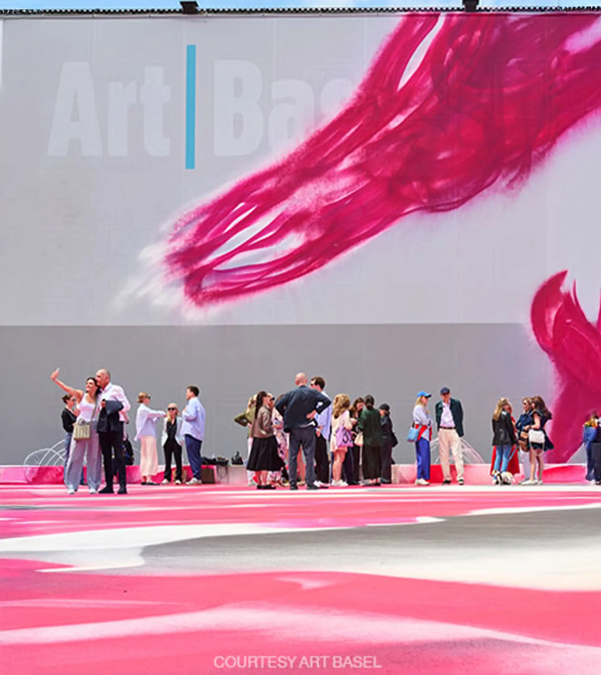 Visitors at Art Basel in Basel standing in front of a large outdoor artwork.