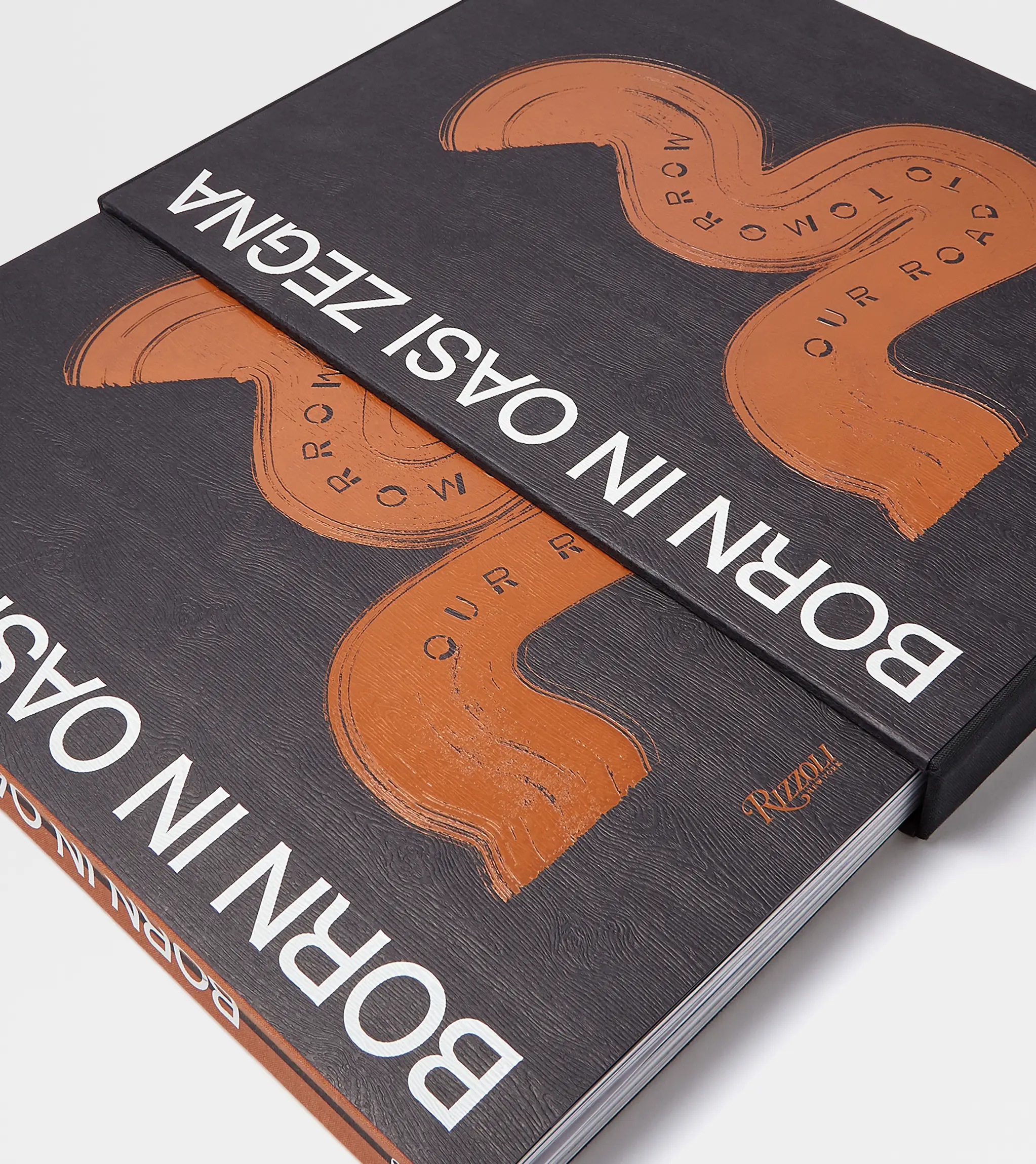 "Born in Oasi Zegna" book with black cover and orange symbol in the center.