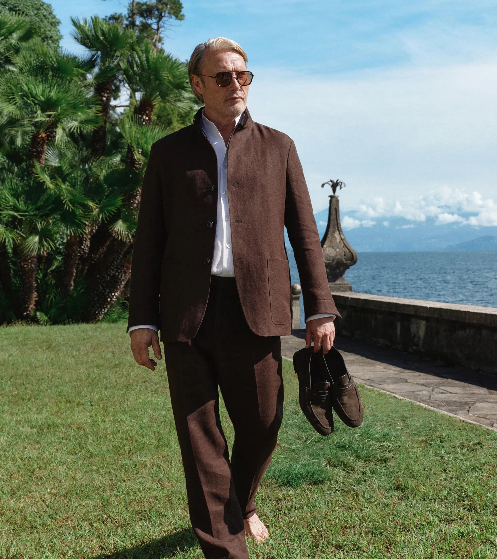 Mads Mikkelsen wearing a refined look from the ZEGNA Spring Summer 2026 collection in a lakeside garden setting.