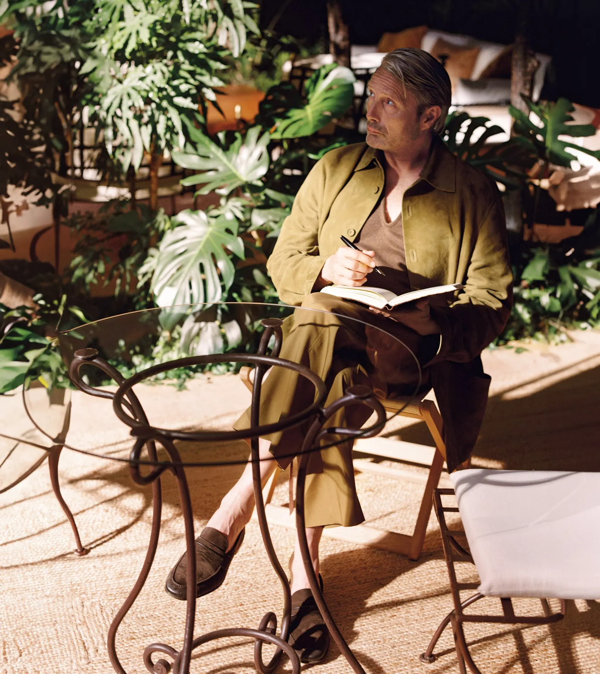 Mads Mikkelsen in a ZEGNA SS26 outfit, sketching ideas in a notebook during a quiet creative moment.