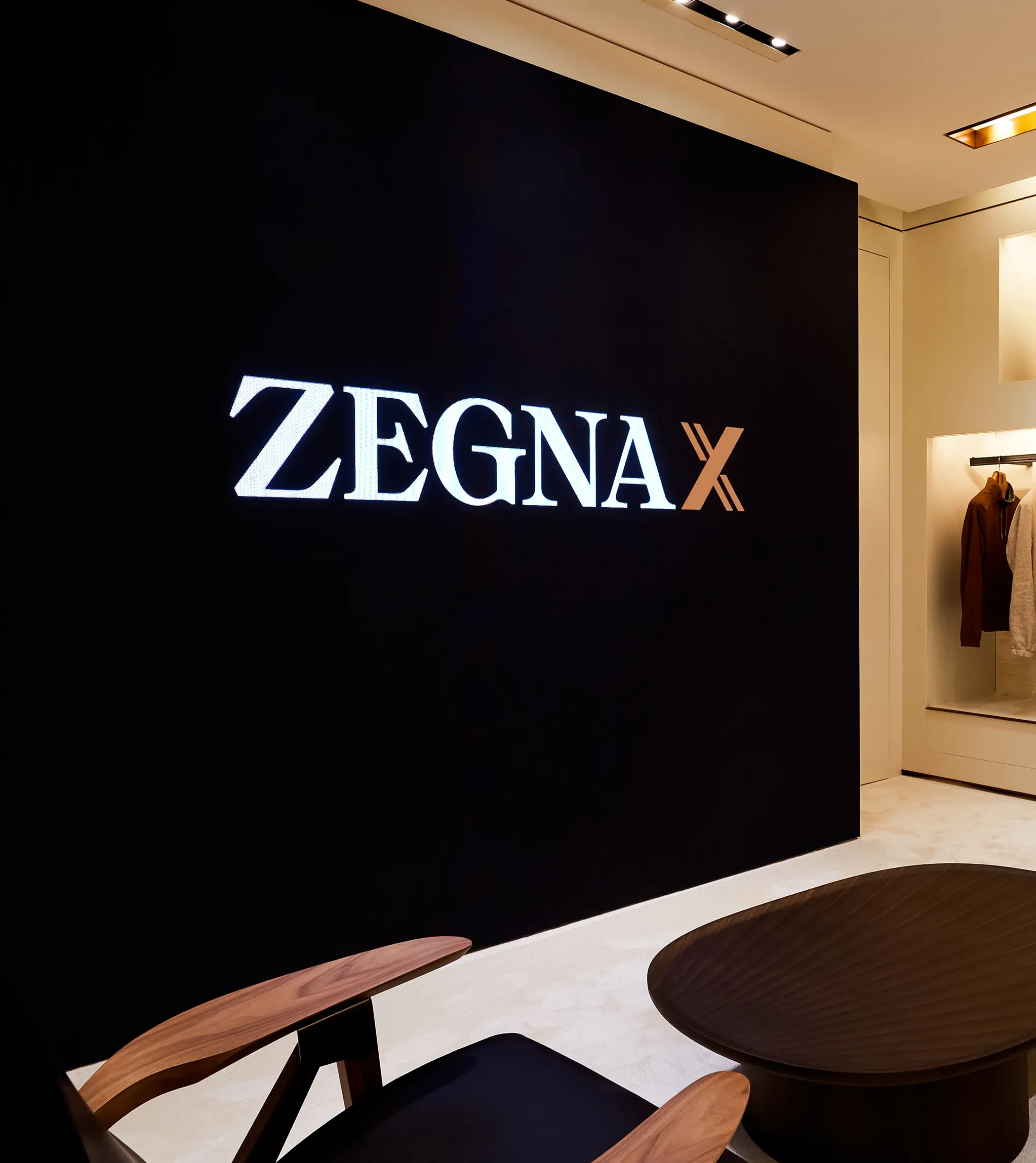 ZEGNA Xロゴのウォールと新しいZEGNA Xワードローブコンフィギュレーターのサービスが見える、ZEGNAブティックの店内。