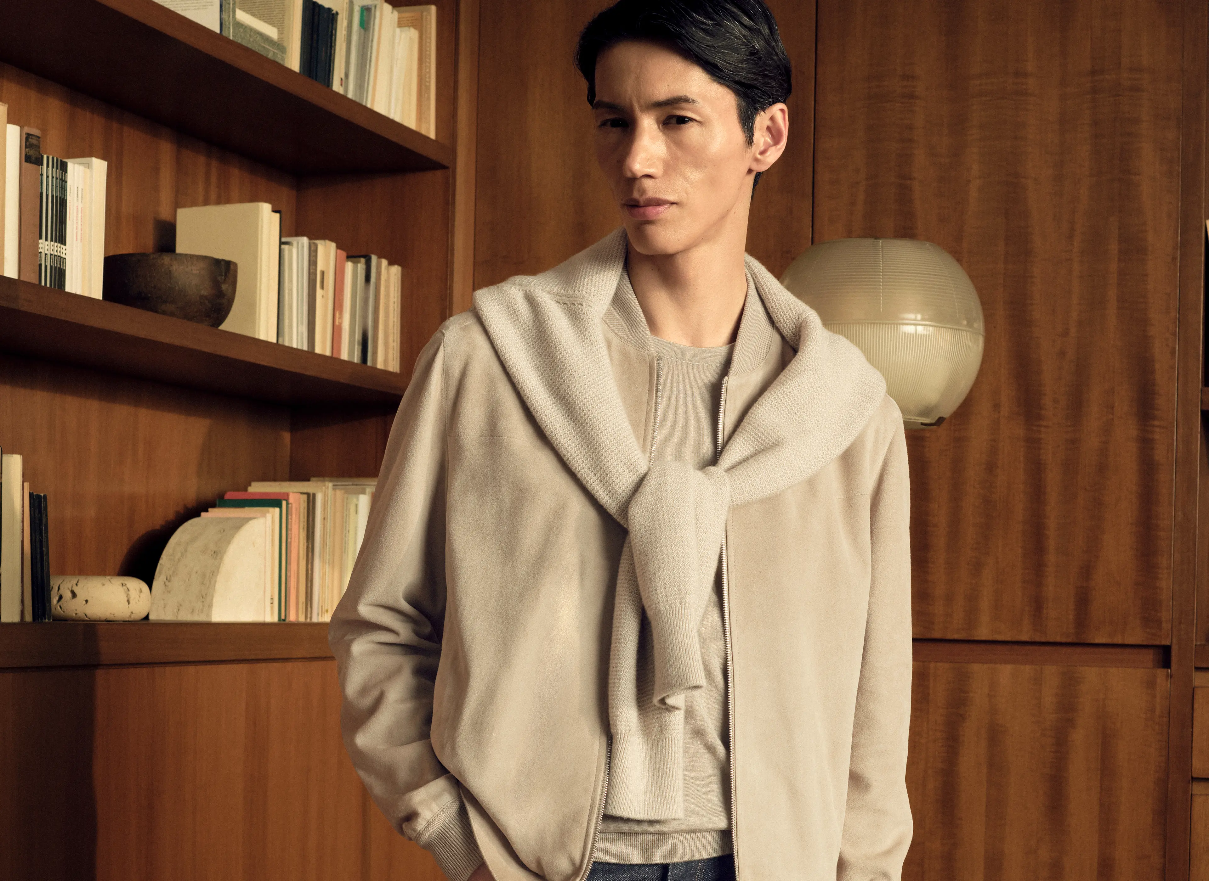 Man wearing the lamb suede bomber in light taupe with an Oasi Cashmere zip mock draped over the shoulders, a Cashseta crewneck and dark blue denim, from the ZEGNA Fall/Winter 2026 collection.