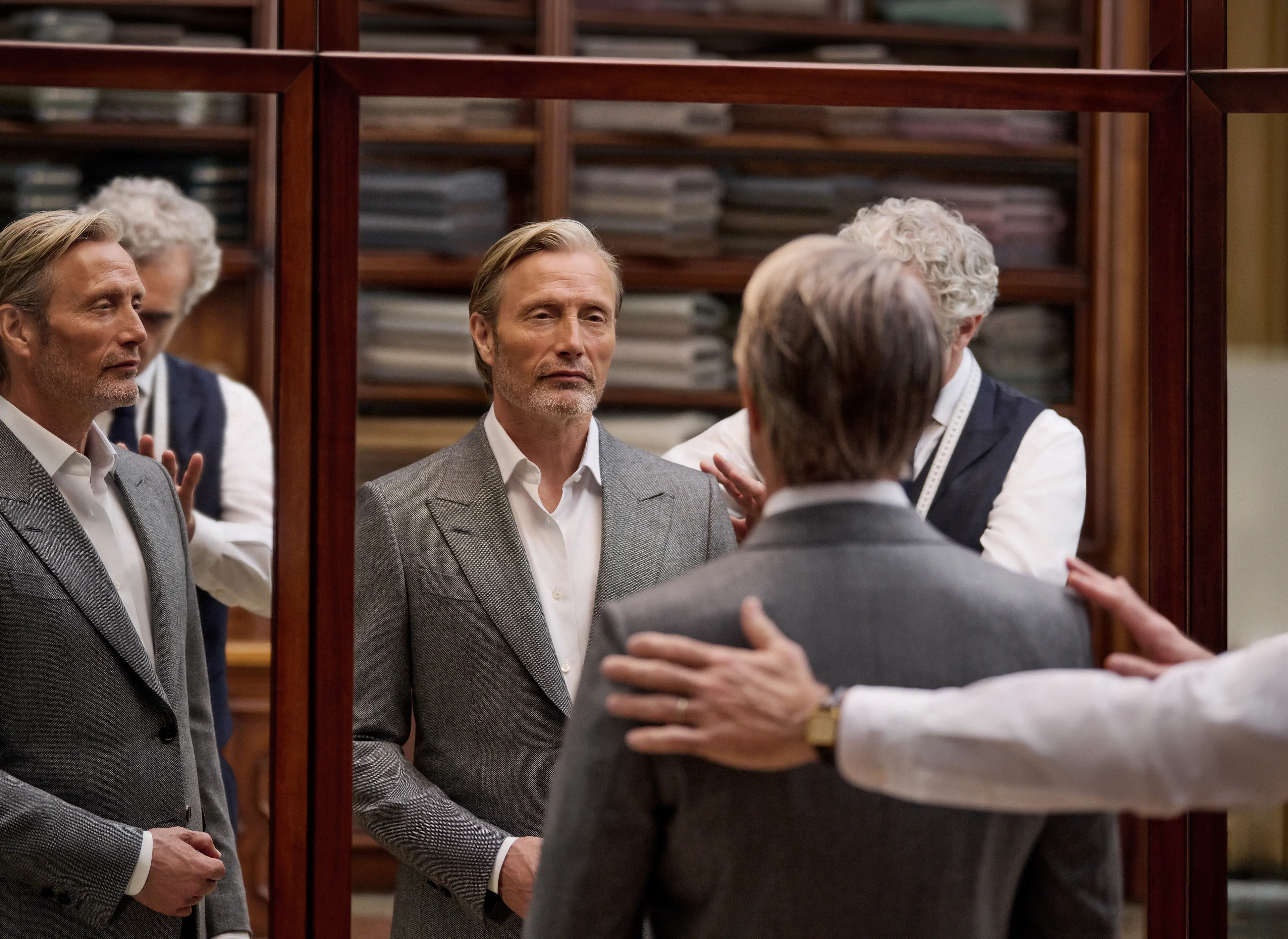 Mads Mikkelsen in a grey tailored suit being fitted by a tailor in an atelier, reflected in the fitting room mirrors, from the ZEGNA Fall/Winter 2026 collection.