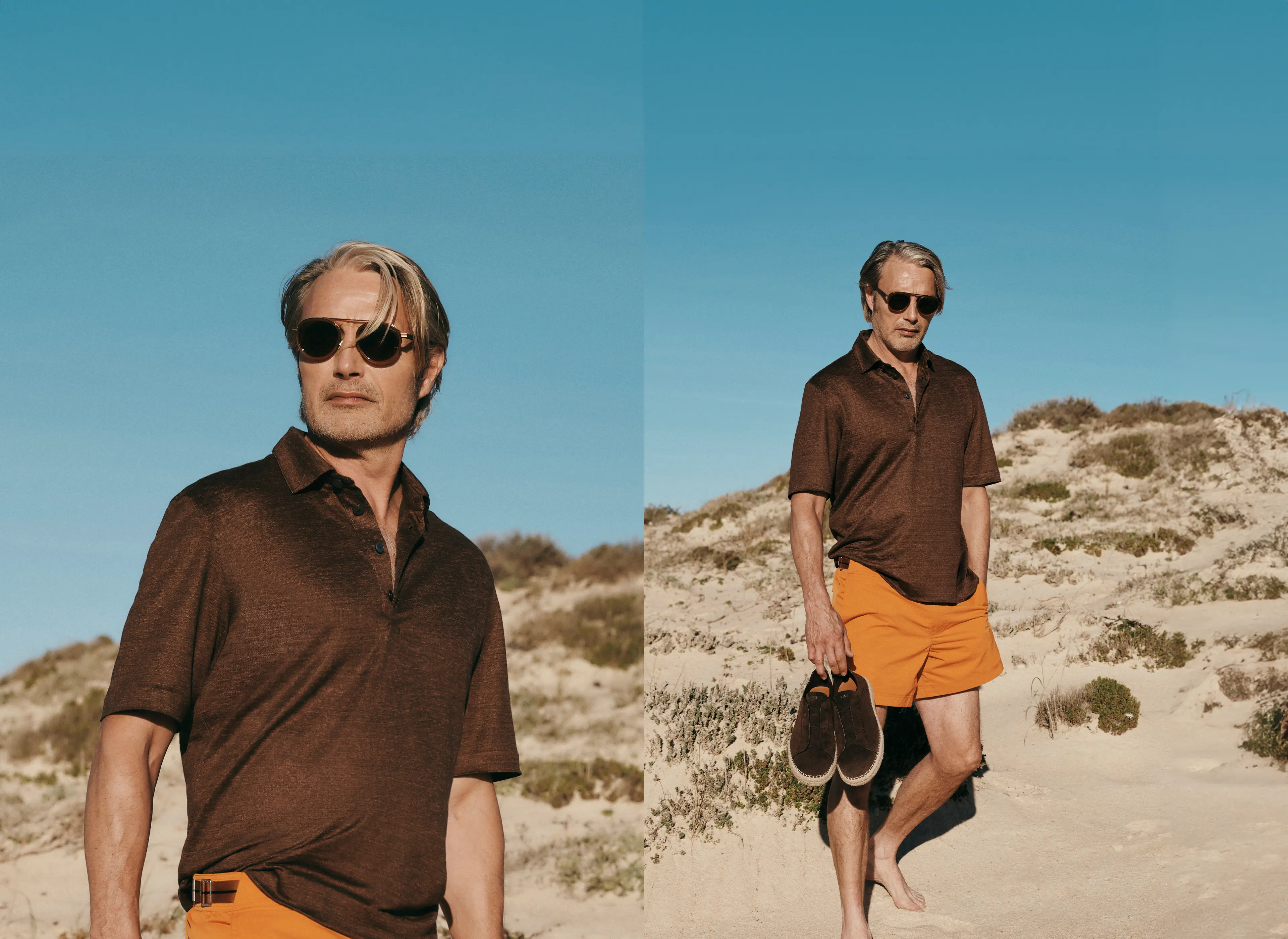 Actor Mads Mikkelsen walking on the beach in a ZEGNA ensemble, featuring a dark brown polo shirt, orange shorts, and sunglasses. 
