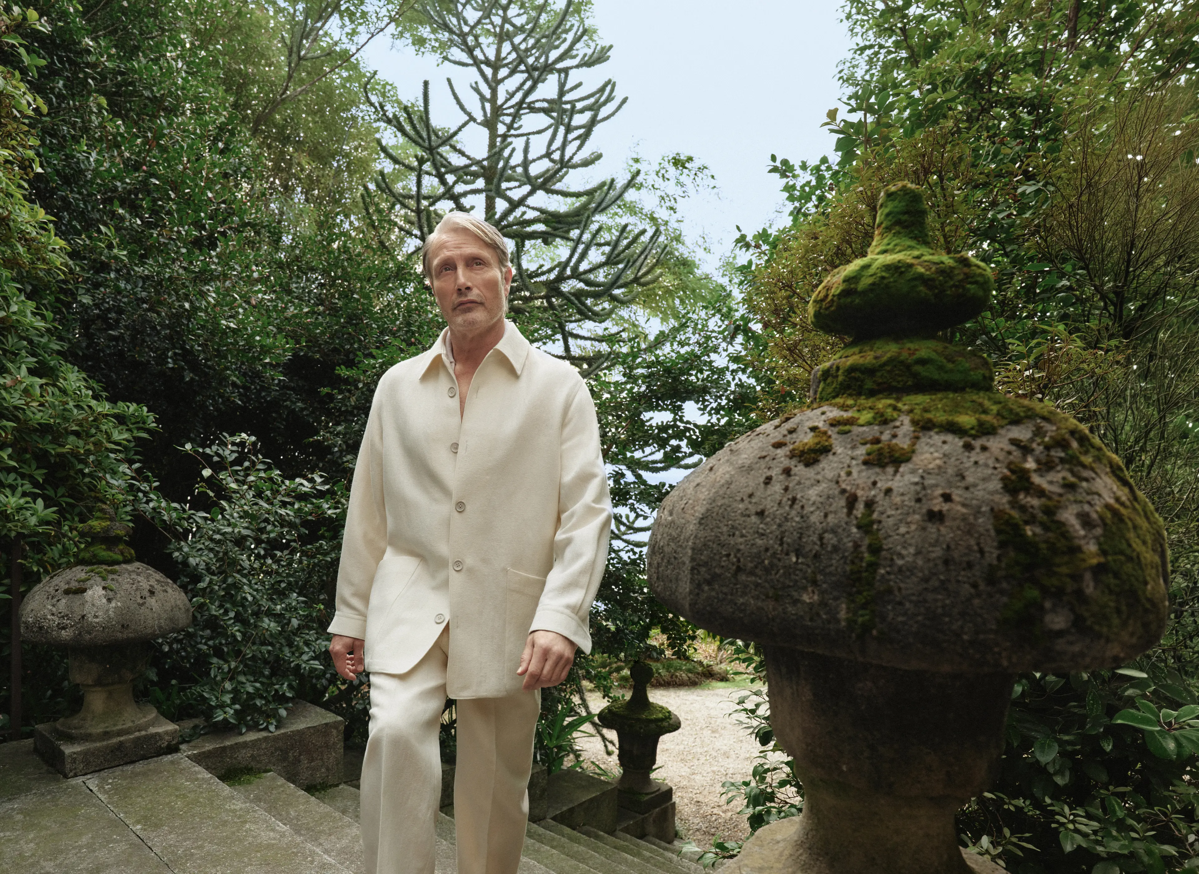 Mads Mikkelsen wearing a refined look from the ZEGNA Spring Summer 2026 collection in a lakeside garden setting.
