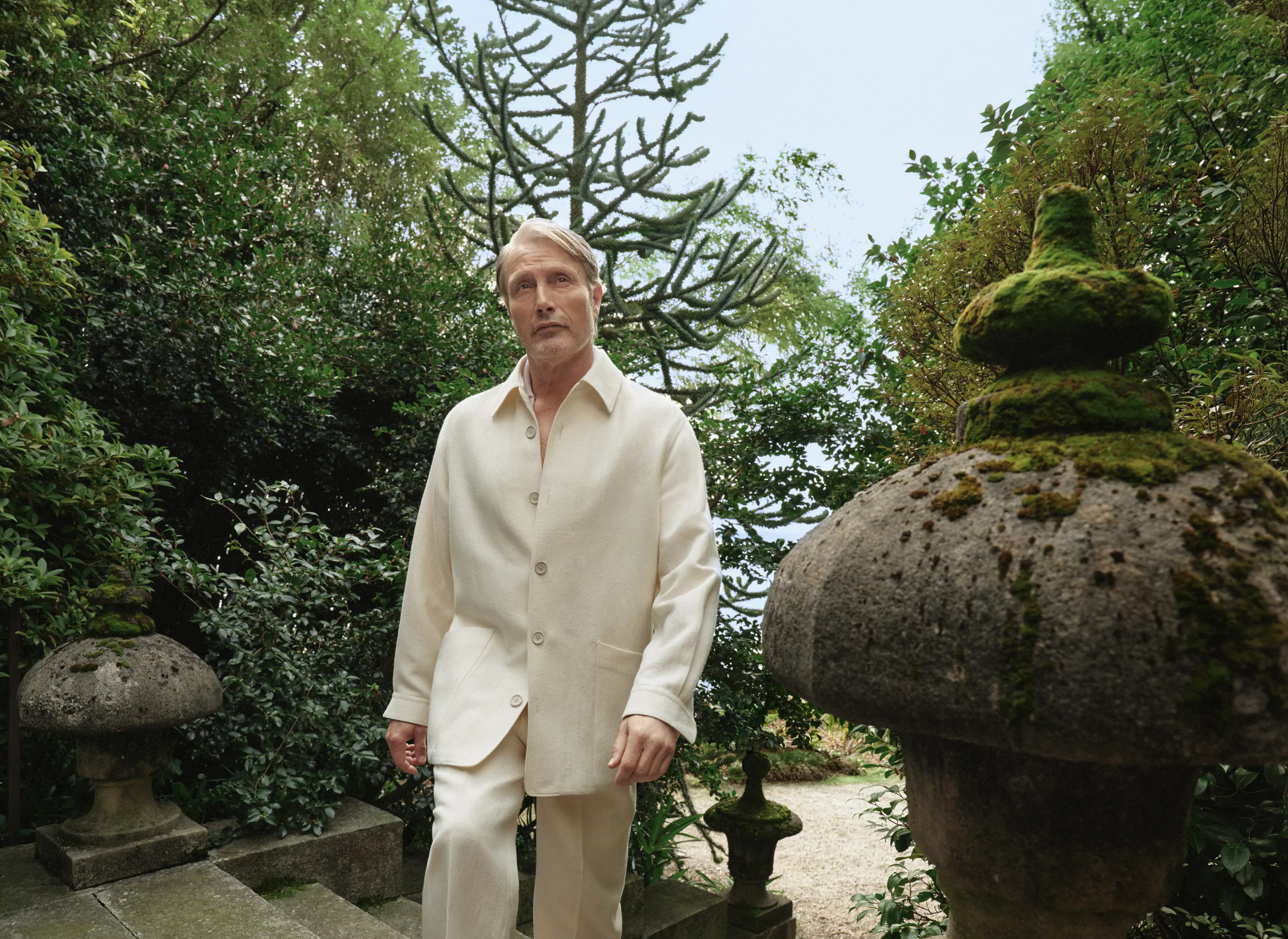 Mads Mikkelsen wearing a refined look from the ZEGNA Spring Summer 2026 collection in a lakeside garden setting.