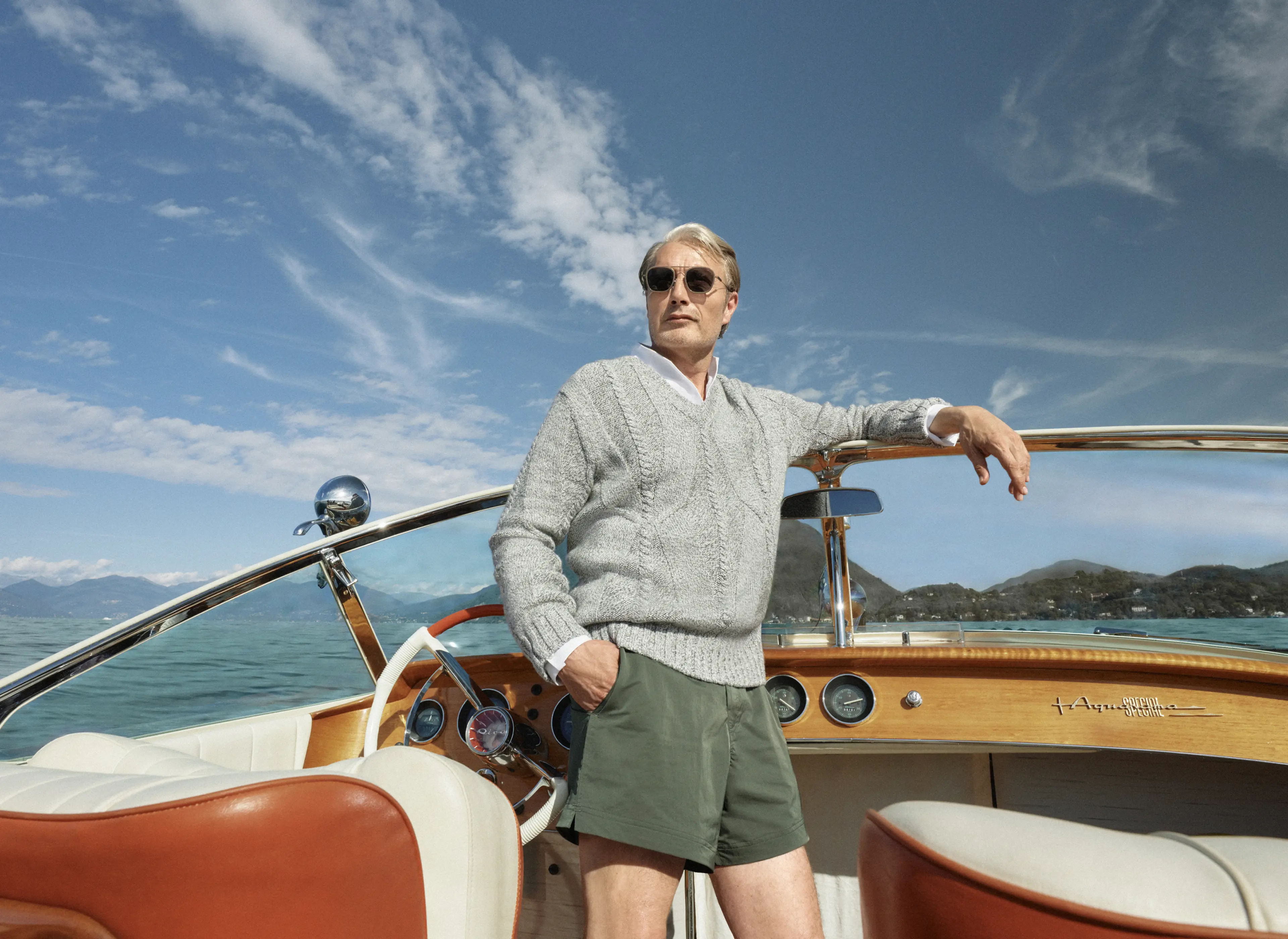 Mads Mikkelsen auf einem Boot in einem Look aus der ZEGNA Frühjahr/Sommerkollektion 2026, bestehend aus einem Pullover mit V-Ausschnitt und der ikonischen Rio Bademode