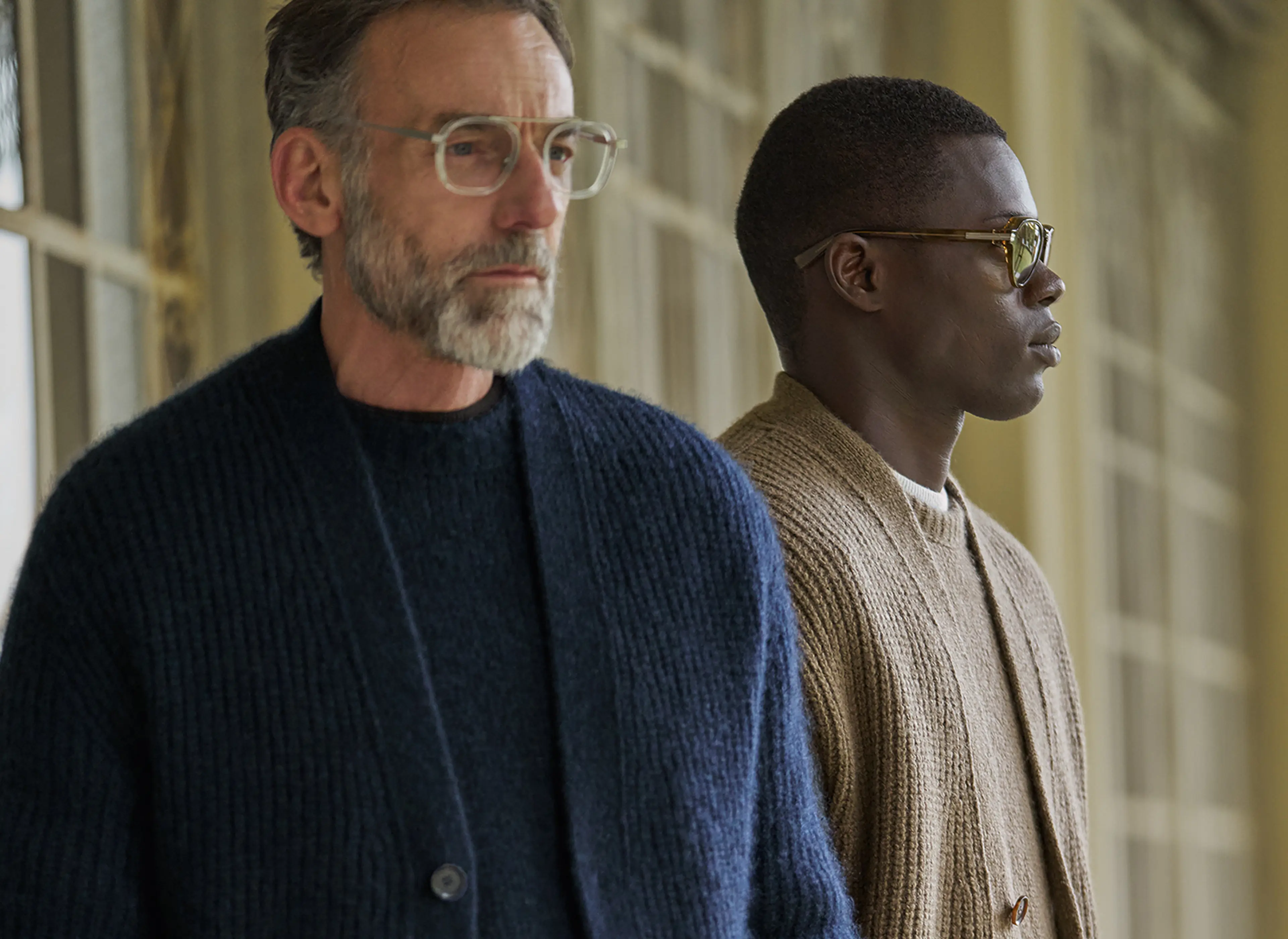 Due uomini indossano look business casual blu e beige, con maglie, cardigan e borse grandi in pelle della nuova collezione ZEGNA.