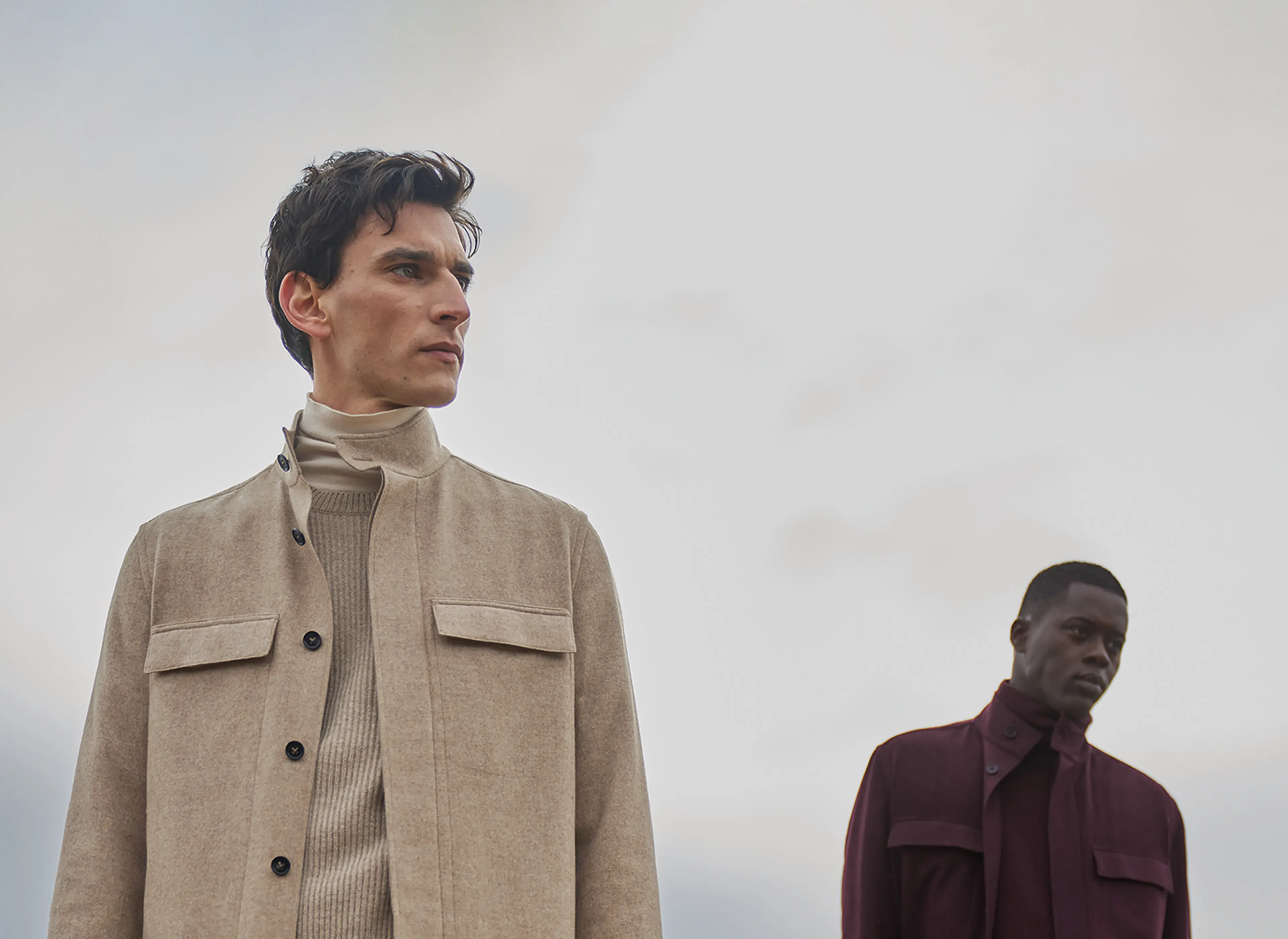 Two men in monochromatic looks, one beige and one deep red, featuring elegant pants, turtlenecks, and jackets from the new ZEGNA fall/winter collection.