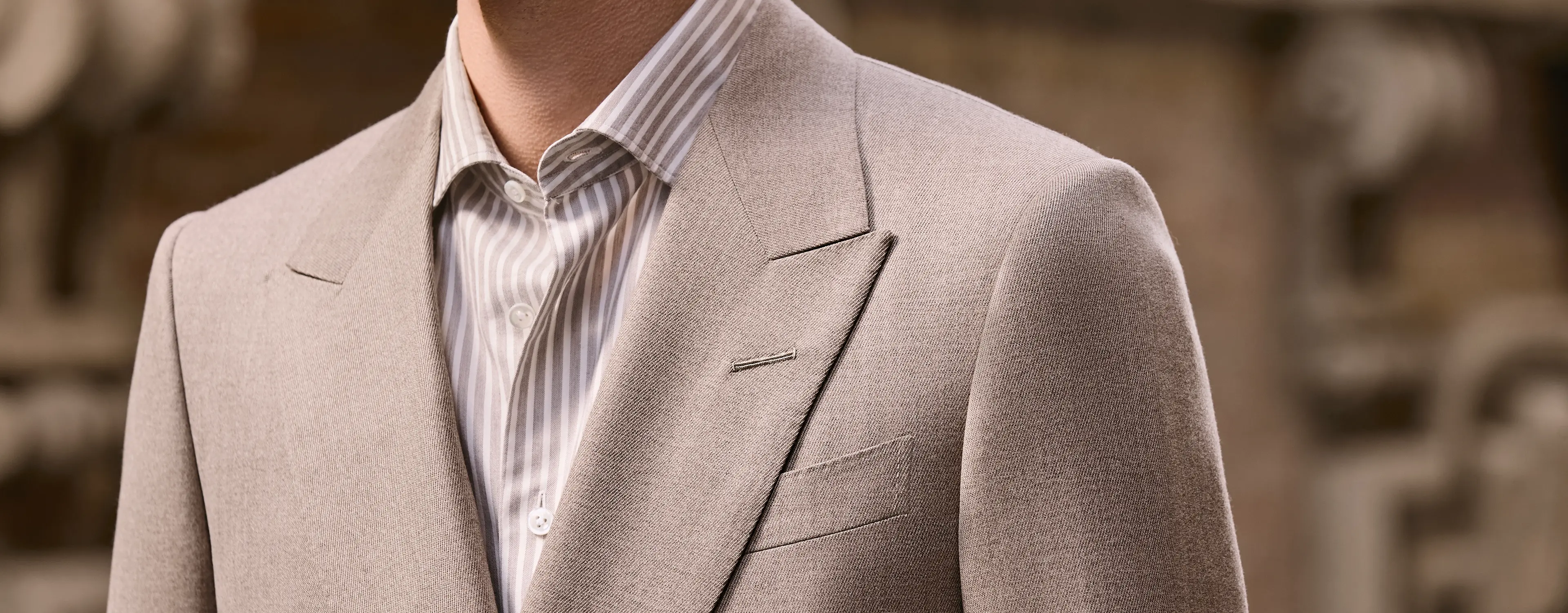 Nahaufnahme einer beigen Anzugjacke von ZEGNA, gestylt mit einem gestreiften Hemd und einem Strick-Layer.