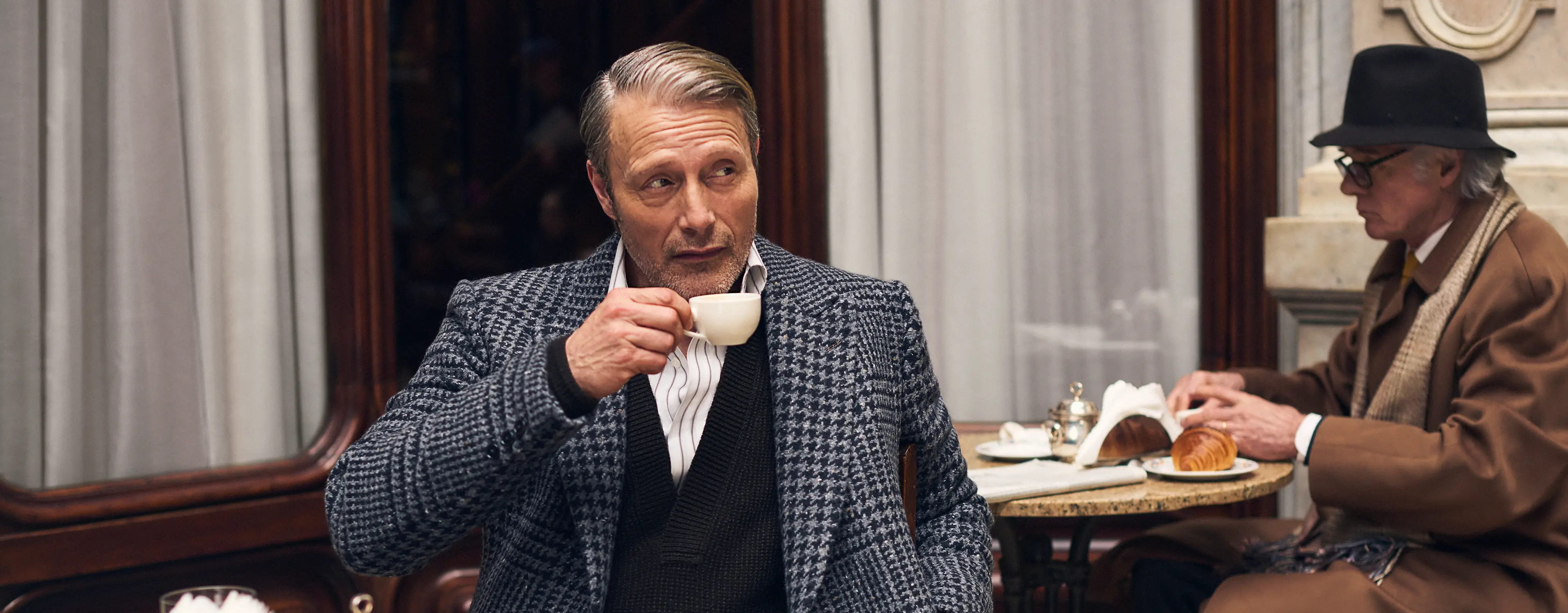 Mads Mikkelsen, seated in a café, wearing a Torino style tailored suit from the ZEGNA FW25 couture collection.