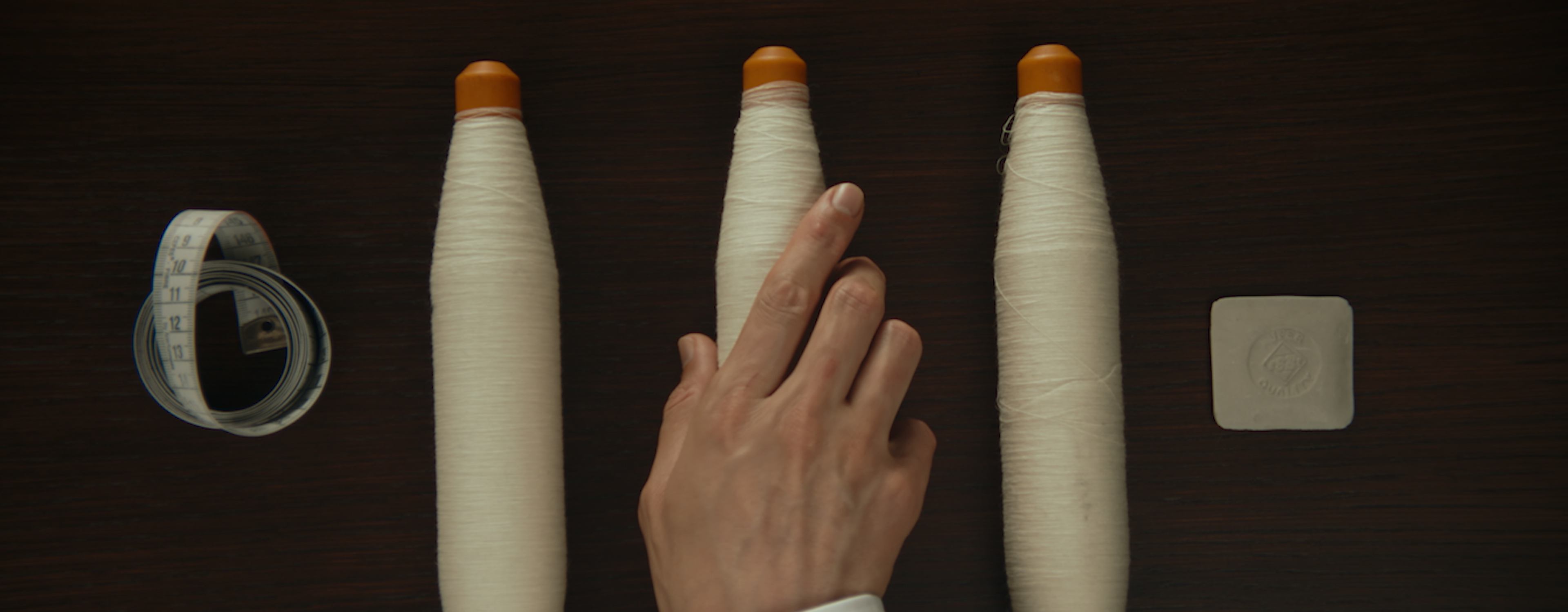 White thread spools, a tailor's measuring tape and a fabric swatch on a dark surface.
