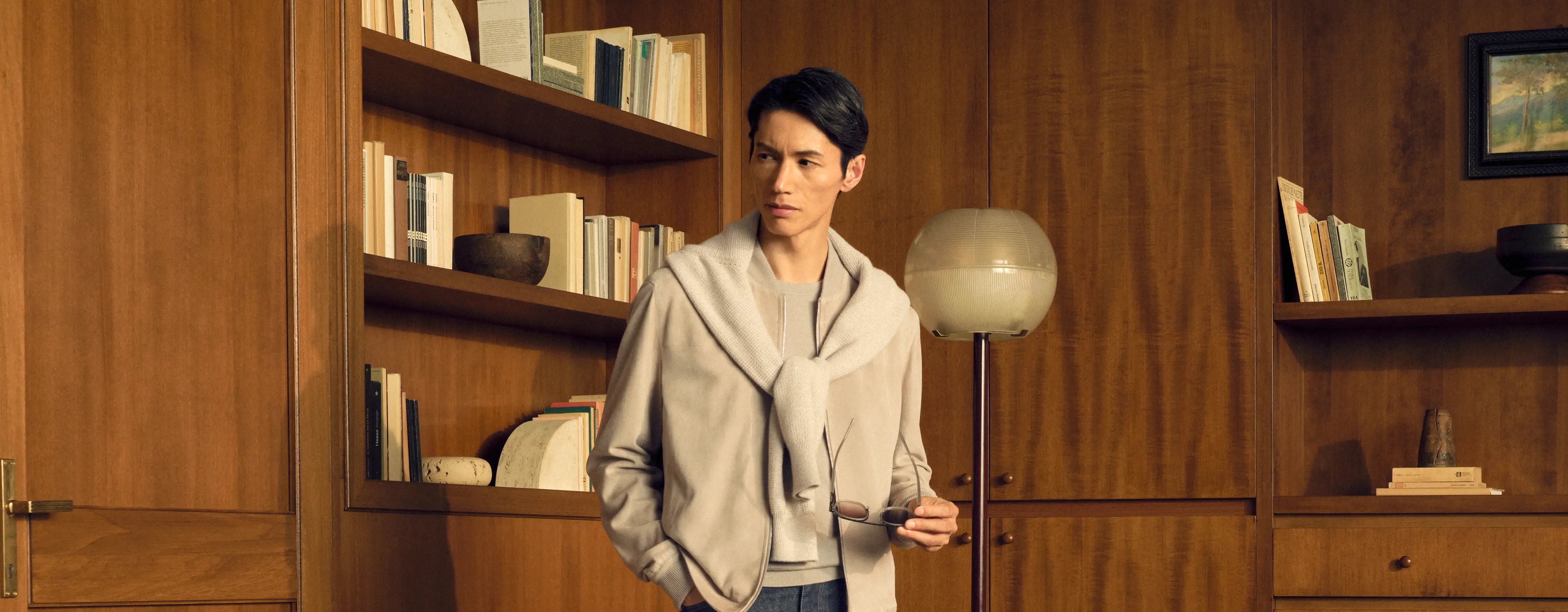 Man in a tonal look wearing the lamb suede bomber in light taupe with an Oasi Cashmere zip mock draped over the shoulders, a Cashseta crewneck and dark blue denim, from the ZEGNA Fall/Winter 2026 collection.
