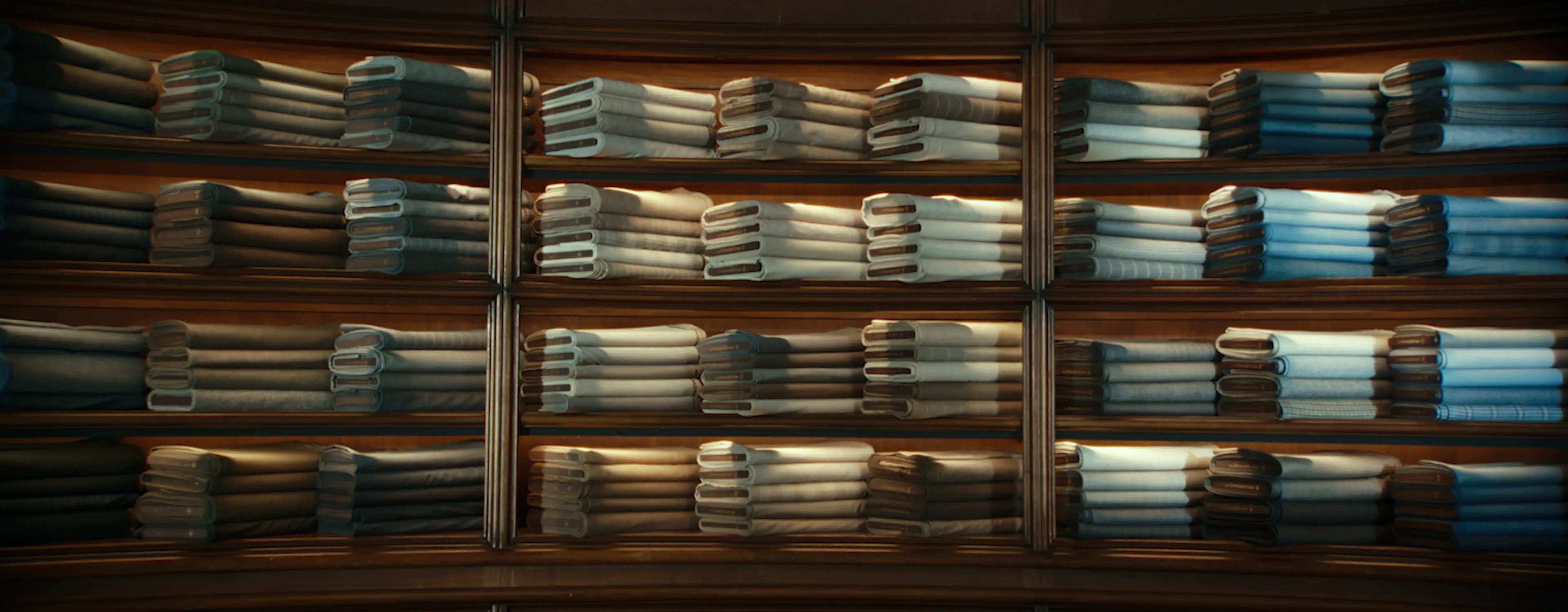 Neatly folded fabrics displayed on illuminated shelves in a ZEGNA tailoring space.