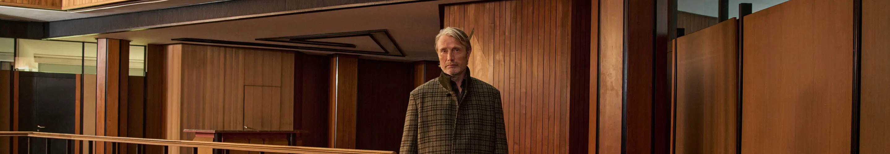 Mads Mikkelsen身穿格纹羊毛夹克与高领内搭，穿行于木饰内部空间，来自ZEGNA 2026秋冬系列。